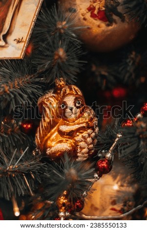 New Year festive magic details. Vintage Christmas toy figurine of funny squirrel hanging on the Christmas tree branches with red beads.