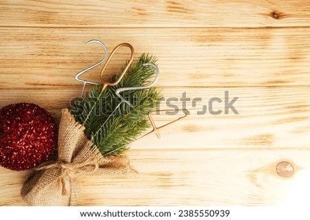 Background for greetings with empty space. Happy new year card. Figures 2024 on a light wooden background with decorative Christmas tree. Top view