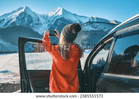Female with mobile phone standing near the car in sunny day. Woman travel exploring, enjoying the view of the mountains, landscape, lifestyle concept winter vacation outdoors.