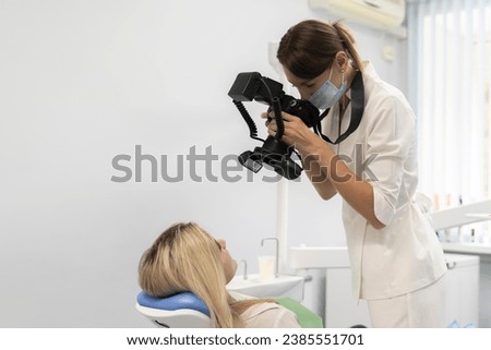 young dentist making shots on a camera of patient's smiling teeth before surgery in her clinic