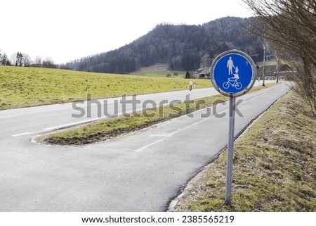 Foot and bicycle path sign in blue color next to an empty main street in late autumn, cloudy sky Bicycle lanes and pedestrian paths are important for people's safety