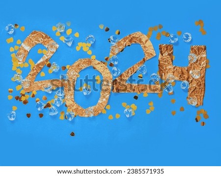 2024 hand made sign made from golden color foil and heart shaped confetti on blue background. New Year celebrations concept.