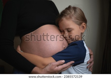 Little cute daughter hugging pregnant mother at home.