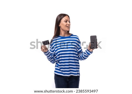 a young cute slender brunette lady with straight hair is dressed in a blue jacket holding a credit plastic card and a smartphone. e-business concept