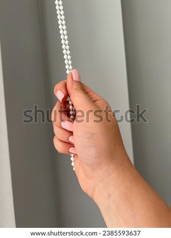 A female hand holding a beaded chain for the blinds