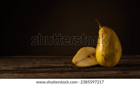 one and a half ripe pears lie on a plank table against the background of a dark wall with a light spot. side view. moody artistic rustic photo with copy space