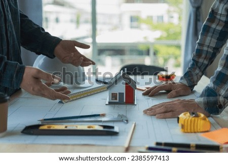 Engineer points to building on blueprint and uses laptop to draw building design project in office Image engineer concept of engineer meeting for architectural project Work with partners