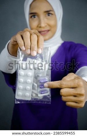 Asian hijab nurse wearing purple medical uniform , holding and ahowing the medicine pills, capsule and tablets.