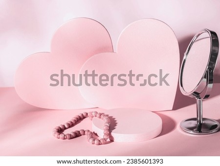 Composition for Valentine's Day or wedding day. Pink hearts on a pastel pink background, a cylindrical podium and a pink necklace and mirror. Product presentation, layout.