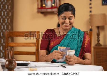 happy smiling middle aged woman counting money or currency notes at home - concept of budgeting, responsible spending and middle class Indian lifestyle Royalty-Free Stock Photo #2385602463