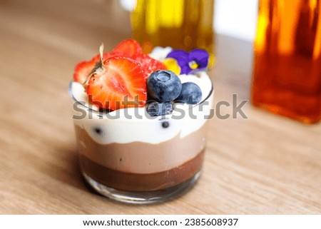Dessert, decorated with fresh fruits and edible flowers, top view. Chocolate and cream layered mousse dessert in a glass cup, selective focus, with blurred background.