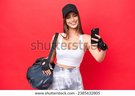 Young beautiful sport woman with sport bag isolated on red background making a selfie
