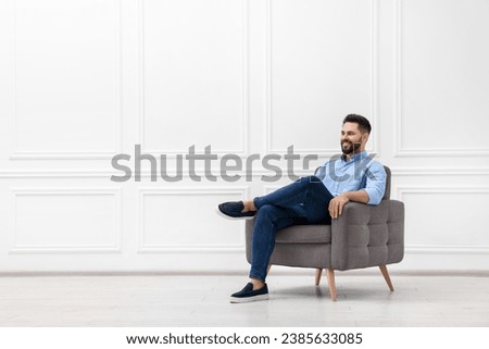 Handsome man sitting in armchair near white wall indoors, space for text Royalty-Free Stock Photo #2385633085