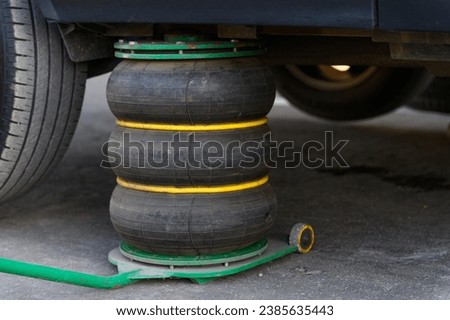 A pneumatic jack supports the vehicle while changing tires. Close-up. Royalty-Free Stock Photo #2385635443