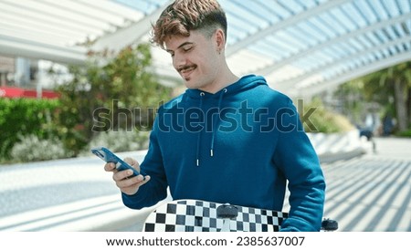 Young hispanic man holding skate using smartphone at park