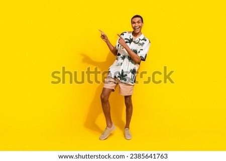 Full length photo of nice young male have fun pointing empty space dressed stylish palms print garment isolated on yellow color background