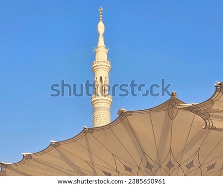 minaret or minaret and large umbrella umbrellas blooming at the nabawi mosque saudi arabia in a sunny day with a blue sky. as background, poster, wallpaper.



