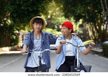 Two Asian boys who are friends ride bicycles in the local park on holiday. They are both happy and having fun. Holiday activity concept. Soft and selective focus.                               