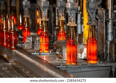 Glass factory, production of glass containers. Molten glass is blown into molds. Robotics in industry. Modern technologies, robotic machines produce products. Technological work at the plant. Royalty-Free Stock Photo #2385654275