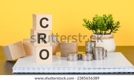 CRO - text on a stack of wooden blocks standing on a notepad with coins, a flower in a pot on a yellow background