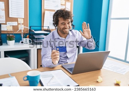 Hispanic young man working at the office doing online shopping looking positive and happy standing and smiling with a confident smile showing teeth 