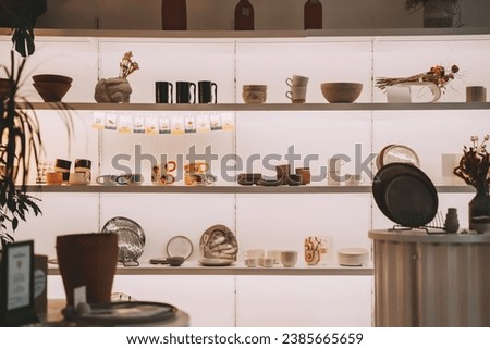 Pottery tablewares on shelves of small art shop. Handmade ceramic pottery objects in art studio workspace. Ceramic Shop's Products. Royalty-Free Stock Photo #2385665659