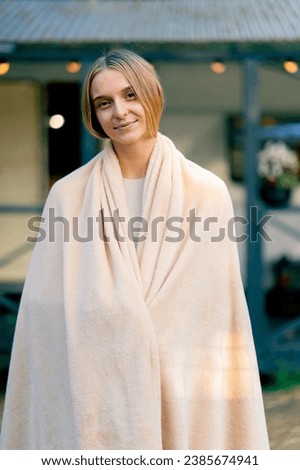 Portrait of a young beautiful smiling girl with a blanket on her shoulders against the background of a mobile home in glamping