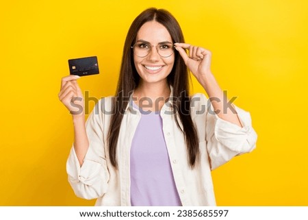 Photo portrait of lovely young lady touch specs hold credit card banker dressed stylish white garment isolated on yellow color background