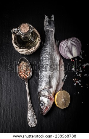 Fresh sea fish lying on dark background with spices. Vertical