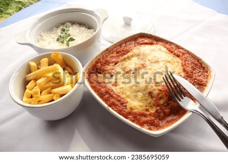Savor a classic Parmesan-crusted steak, accompanied by golden French fries and fluffy white rice, delivering a hearty and satisfying dining experience. Royalty-Free Stock Photo #2385695059
