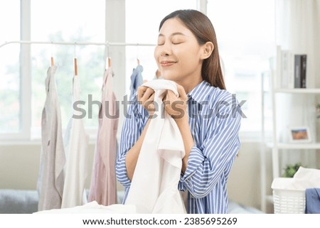 Feel softness, hygiene. Smile asian young woman touching fluffy white shirt smelling fresh clean clothes, pretty girl comfort sniff after washing laundry. Household work at home, chore of maid concept Royalty-Free Stock Photo #2385695269