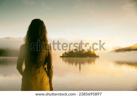 Woman in yellow dress watching a sunrise among the fog on the shores of Lake Bled, Slovenia VII Royalty-Free Stock Photo #2385695897