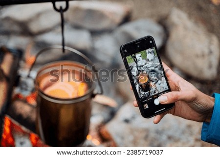 Taking pictures on the phone of a pot on the fire, a female hand with a smartphone filming the food cooking process, art photography, food photo. High quality photo