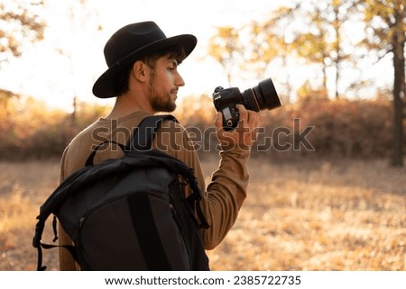 Nature photography concept. Professional nature photographer with digital camera and autumn forest on background. Copy space