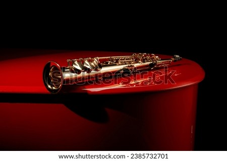 Straight saxophone on the lid of a red piano. Copy space. Shallow depth of field.  Royalty-Free Stock Photo #2385732701