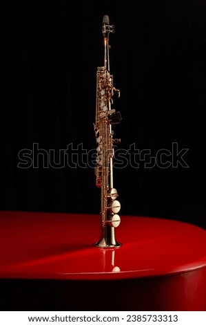 Soprano saxophone on the lid of a red piano against black background. Copy space. Shallow depth of field.  Royalty-Free Stock Photo #2385733313