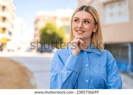 Young pretty blonde woman at outdoors With glasses and thinking while looking up