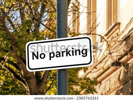 Large no parking traffic sign outside on urban street with trees in the back