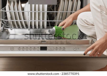 female hand pours rinse aid into the dishwasher compartment in modern white kitchen Royalty-Free Stock Photo #2385770391
