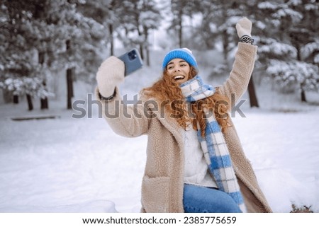 Happy woman takes a selfie using a smartphone in a snowy winter forest. Concept of blogging, travel, weekend. Active lifestyle.