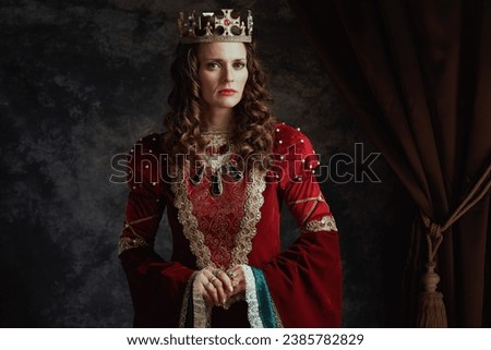 medieval queen in red dress with crown on dark gray background. Royalty-Free Stock Photo #2385782829
