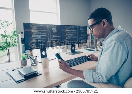 Photo of smart clever young man wear blue informal shirt coding computer editing database code program typing phone in workshop office