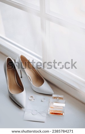 Close-up view of Wedding details. Bride elegance shoes, rings, parfume and invation layflat on white windowsill  