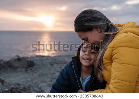 Mother and daughter together in front of the sea watching a sunset. Concept: together, lifestyle, love