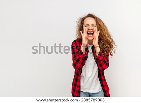 Attractive curly woman standing in front of white background in studio and shouts cupping her hands around the mouth.