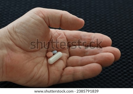 A hand holding a daily dose of three tablets. The tablets are white, rose and blue. GoranOfSweden Royalty-Free Stock Photo #2385791839