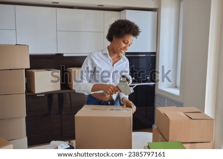 people, moving new place and repair concept - happy african american young woman with many cardboard boxes sitting on floor at home Royalty-Free Stock Photo #2385797161