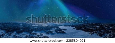 Very wide scenic aerial panorama on frozen lake, mountains with snow mobile traces, northern green lights over mountains. Scandinavian night winter landscape, Norway, Sweden Royalty-Free Stock Photo #2385804021