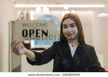 Woman store owner turning open sign broad through the door glass and ready to service. Small business woman owner turning the sign for the reopening
