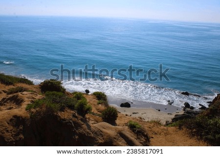 a beautiful summer landscape at Point Dume State Beach with vast blue ocean water and waves rolling into the beach, rocks along the cliffs and blue sky in Malibu California USA Royalty-Free Stock Photo #2385817091